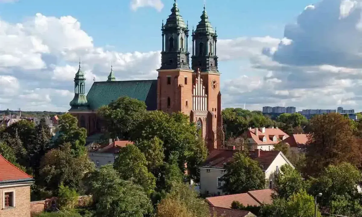 Majestatyczna poznańska katedra z zielonym dachem i dwiema wieżami góruje nad drzewami i budynkami.