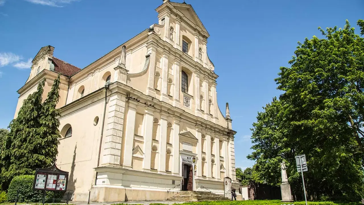 Jasny kościół Karmelitów w Poznaniu z zielenią i błękitnym niebem.