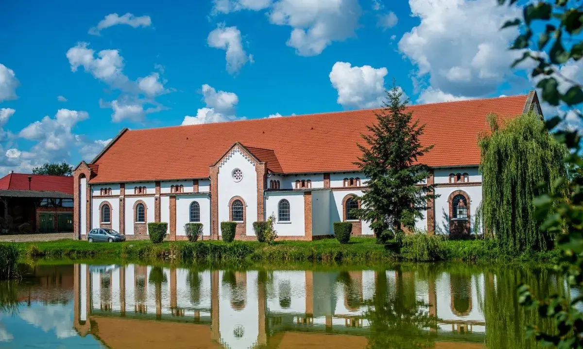 Pałac w Racocie z czerwonym dachem i białymi ścianami odbija się w spokojnej tafli wody.