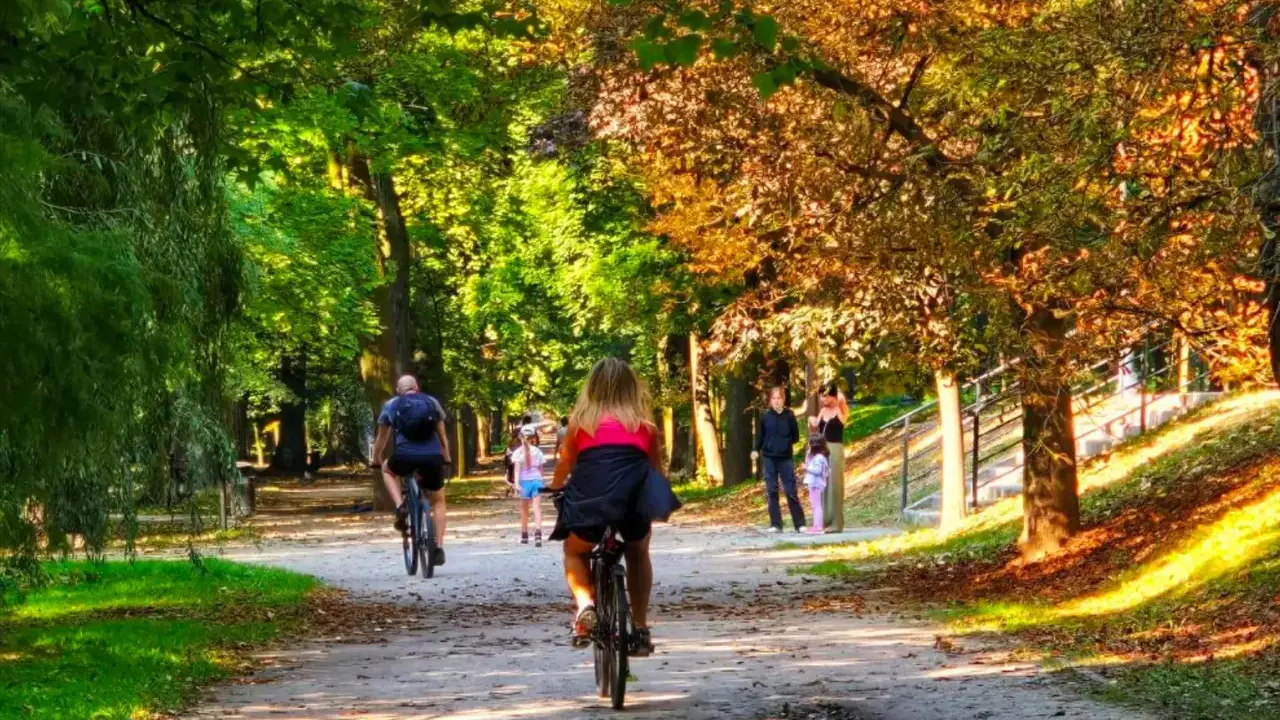 Kalisz wydarzenia weekend: ludzie jeżdżą na rowerach i spacerują alejkami parku w jesiennym słońcu.