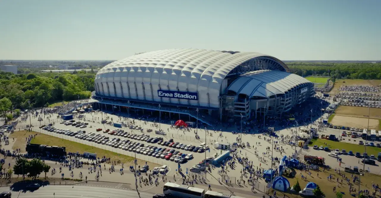Enea Stadion z lotu ptaka, otoczony parkingami i tłumem ludzi.