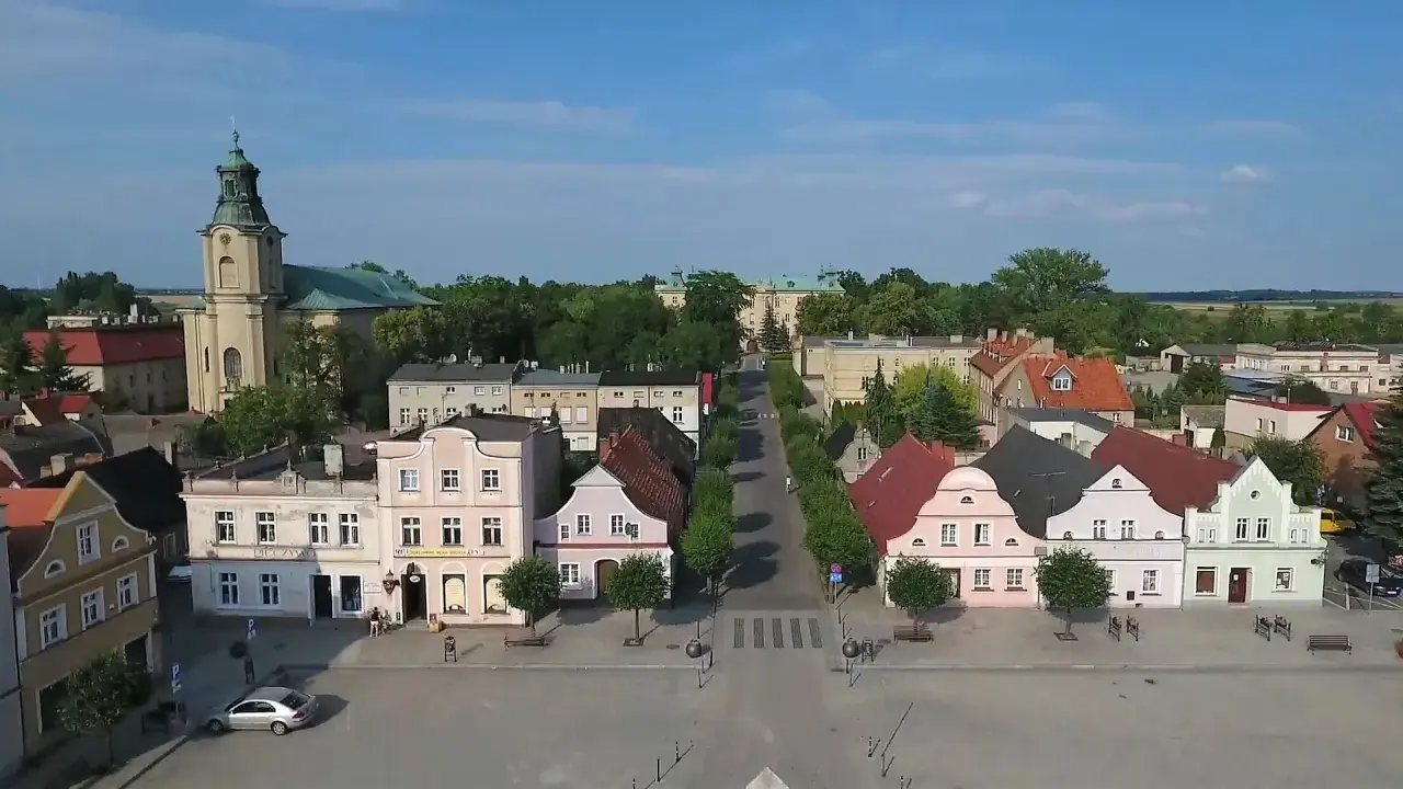 Rydzyna atrakcje: malowniczy rynek z kolorowymi kamieniczkami, kościołem i pałacem w tle.