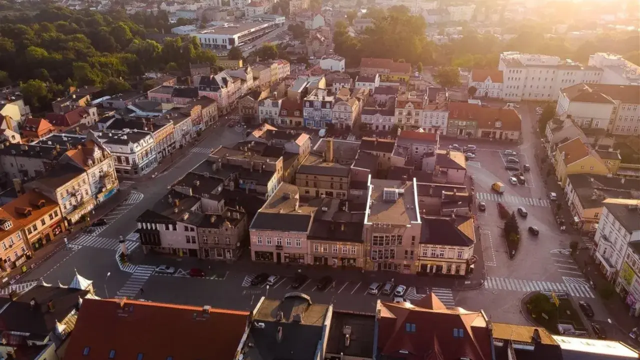 Widok z lotu ptaka na szamotuły rynek z kolorowymi kamienicami i ulicami oświetlonymi zachodzącym słońcem.