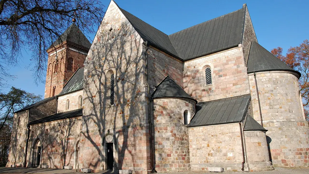 Kamienna budowla z ceglaną wieżą, z cieniem drzew na ścianach, w stylu romańskim, przed gotykiem.