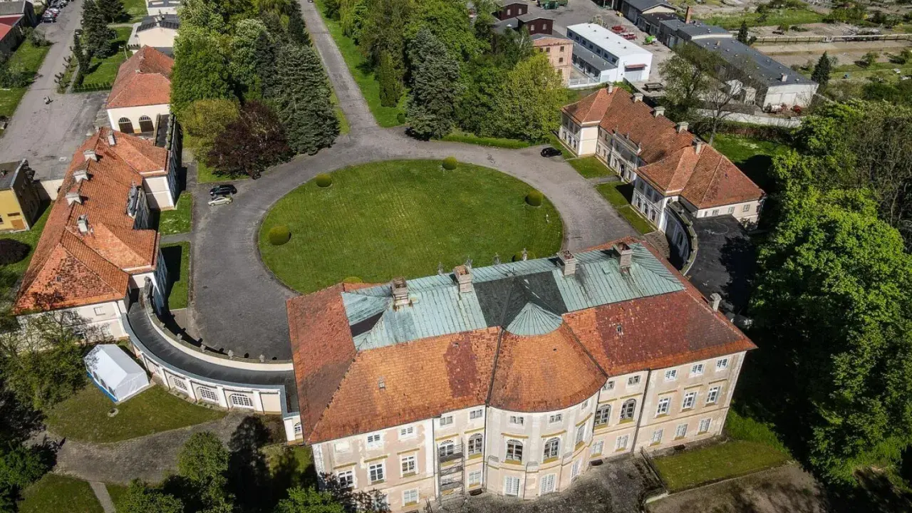 Pałac w Pawłowicach z lotu ptaka, otoczony zielenią i innymi budynkami.