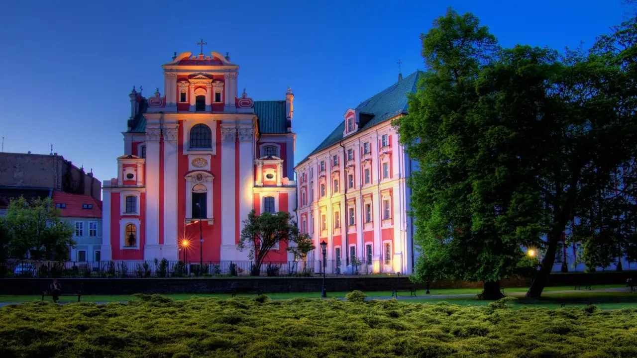 Piękna poznańska trasa spacerowa z zabytkowymi budynkami oświetlonymi wieczorem i bujną zielenią.