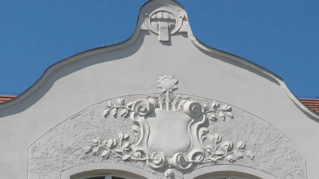 Ozdobny detal architektoniczny w stylu secesja w Poznaniu: tarcza z motywami roślinnymi i groteskowa twarz na szczycie.