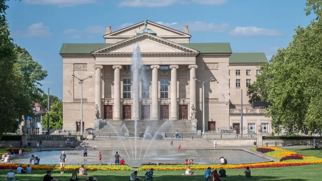 Teatr Wielki w Poznaniu z fontanną i ludźmi odpoczywającymi na trawie to jedne z fajnych miejsc w Poznaniu na spotkanie.