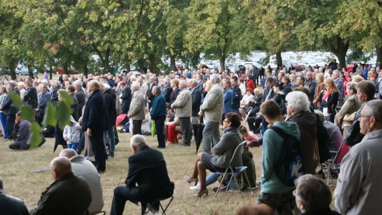 Tłum ludzi zgromadzony na trawie, drzewa w tle. Odpust w Bieniszewie przyciągnął wielu wiernych.