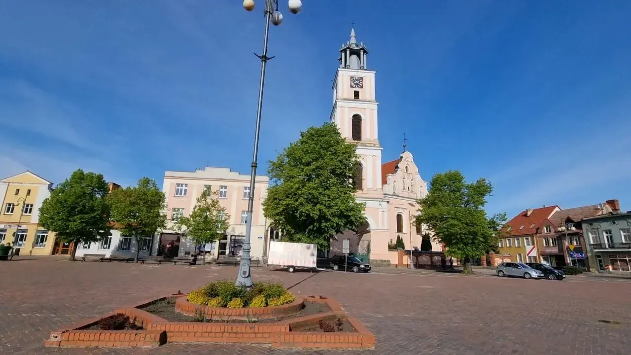 Rynek w Chodzieży Wielkopolskiej z kościołem i kamienicami. Słoneczny dzień, błękitne niebo.