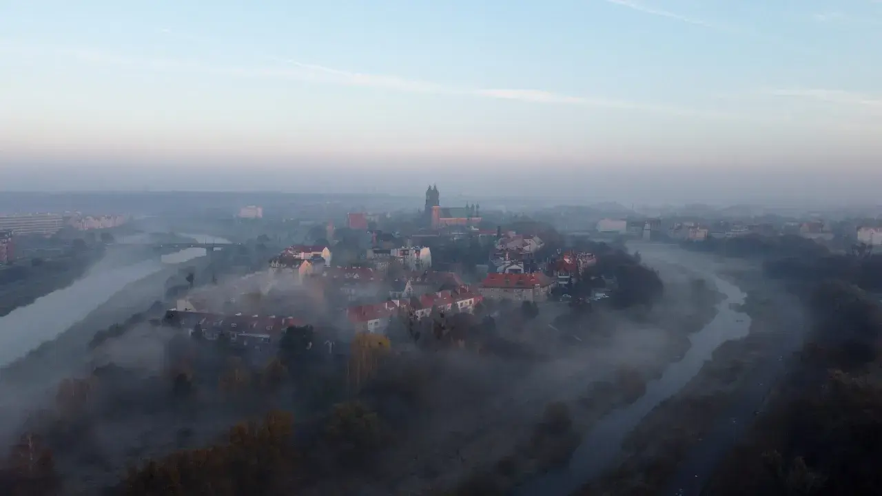 Mglisty poranek nad rzeką, wyłaniający się z mgły **Ostrów Tumski Poznań** z katedrą i zabytkową zabudową.