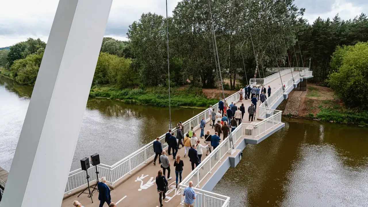 Uroczyste otwarcie kładki owińskiej. Ludzie spacerują po nowoczesnym moście wiszącym nad rzeką, otoczonym zielenią.