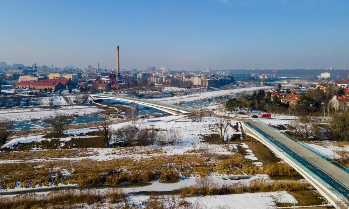 Zimowy krajobraz z nowoczesnymi mostami berdychowskimi, rzeką i panoramą miasta w tle.