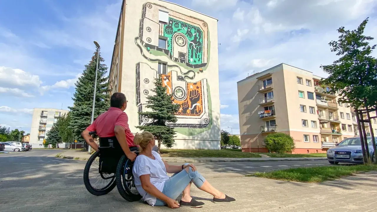 Para w Jarocinie podziwia mural na bloku. On na wózku, ona siedzi obok.