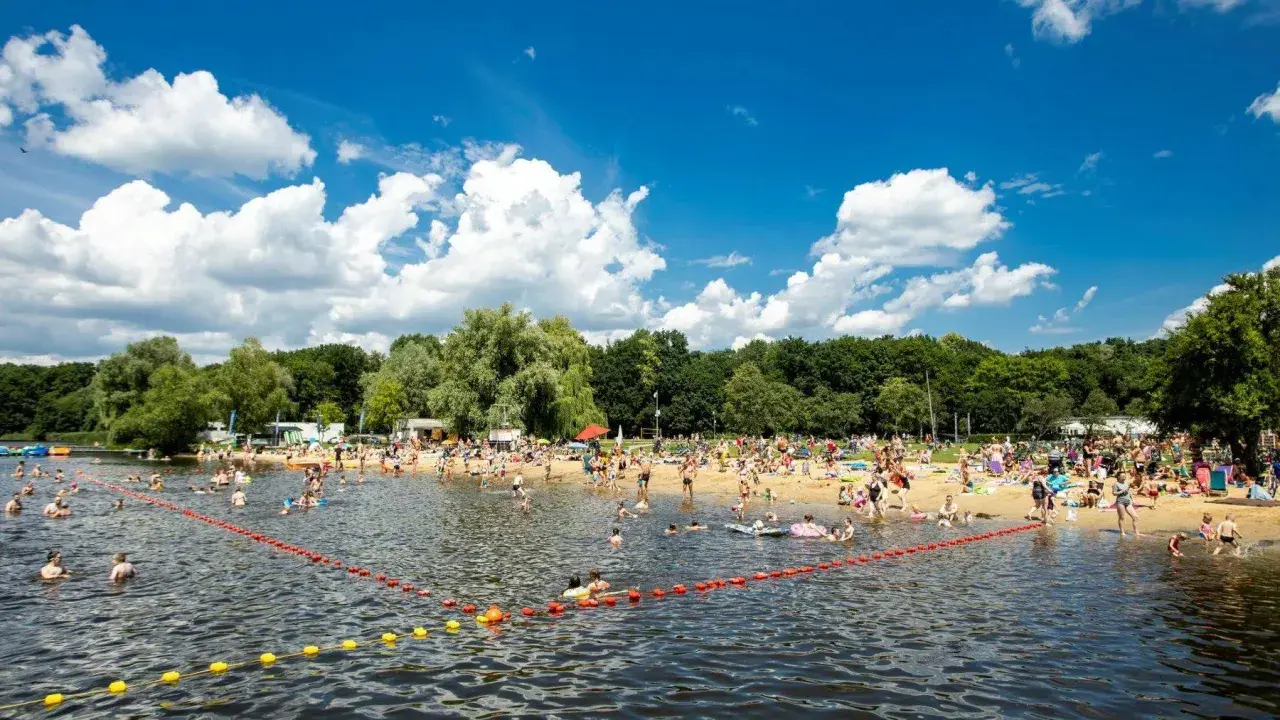 Tłum ludzi odpoczywa na plaży i kąpie się w jeziorze w Poznaniu. Słoneczny dzień, błękitne niebo z chmurami.