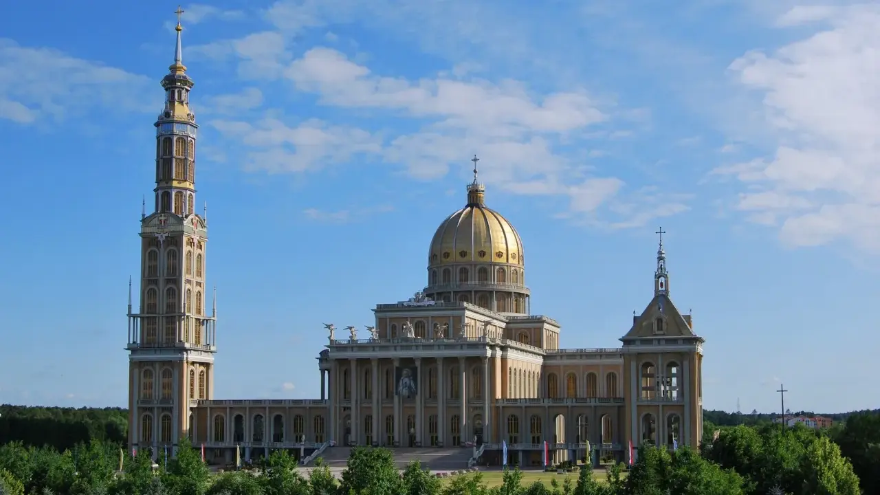 Imponujące sanktuarium koło Konina z wysoką wieżą i złotą kopułą, otoczone zielenią.