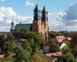 Majestatyczna poznańska katedra z zielonym dachem i dwiema wieżami góruje nad drzewami i budynkami.