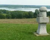 Kamienny, wielki grzyb z inskrypcją stoi na wzgórzu. W tle jezioro i las.