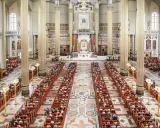 Wielka bazylika w Licheniu Nowym wypełniona wiernymi. Długie ławy zapełnione ludźmi, majestatyczne kolumny i ołtarz w tle.