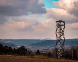 Wieża widokowa na tle malowniczego krajobrazu z pagórkami i chmurami.