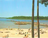 Słoneczny dzień nad jeziorem Niedzięgiel. Ludzie odpoczywają na plaży i pływają, a na wodzie unosi się platforma rekreacyjna.
