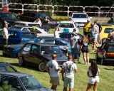 Zlot fanów motoryzacji w Łobżenicy. Wiele samochodów, ludzie oglądają auta, atmosfera piknikowa.