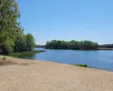 Piękny dzień nad jeziorem w Wielkopolsce. Piaszczysta plaża, spokojna woda i zielone drzewa tworzą idealne miejsce na wypoczynek.