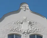 Ozdobny detal architektoniczny w stylu secesja w Poznaniu: tarcza z motywami roślinnymi i groteskowa twarz na szczycie.