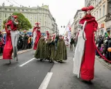 Parada z okazji św. Marcina. Postacie na szczudłach w czerwonych strojach i dzieci w zielonych płaszczach idą ulicą. Legenda o św. Marcinie ożywa.
