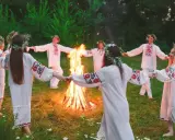 Ludzie w tradycyjnych strojach tańczą w kręgu wokół ogniska, celebrując święto Kupały.