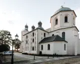 Majestatyczna fara w Grodzisku Wlkp. z charakterystycznymi kopułami i wieżami, otoczona brukowanym placem i zabytkowymi latarniami.