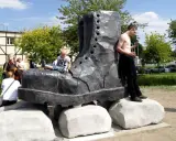 Pomnik glana w kształcie gigantycznego buta, na którym siedzi chłopiec. Obok stoi mężczyzna.