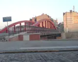 Czerwony most Biskupa Jordana z kłódkami na balustradach, otoczony kamienicami.