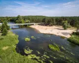 Malownicza plaża nad jedną z wielkopolskich rzek, z mostem i lasem w tle. Idealne miejsce na wypoczynek.