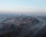 Mglisty poranek nad rzeką, wyłaniający się z mgły **Ostrów Tumski Poznań** z katedrą i zabytkową zabudową.
