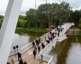 Uroczyste otwarcie kładki owińskiej. Ludzie spacerują po nowoczesnym moście wiszącym nad rzeką, otoczonym zielenią.