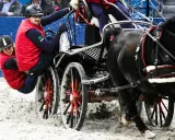 Para jeźdźców w czerwonych kamizelkach w akcji podczas Cavaliady. Dynamiczna jazda zaprzęgiem po piaszczystym torze.