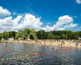 Tłum ludzi odpoczywa na plaży i kąpie się w jeziorze w Poznaniu. Słoneczny dzień, błękitne niebo z chmurami.