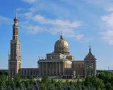 Imponujące sanktuarium koło Konina z wysoką wieżą i złotą kopułą, otoczone zielenią.