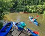 Rodzina pływa kajakami po rzece Prośnie, otoczonej bujną zielenią.