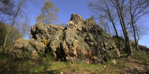 Skalisty pagórek, gdzie według legendy diabeł zostawił swój kamień. Drzewa o nagich gałęziach otaczają go, a niebo jest błękitne.
