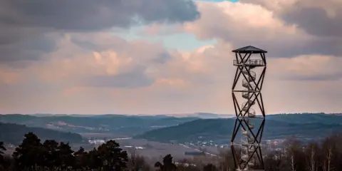 Wieża widokowa na tle malowniczego krajobrazu z pagórkami i chmurami.