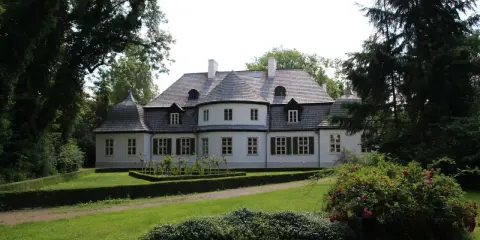 Malowniczy dwór w Koszutach otoczony zielenią. Klasyczna architektura z wieżyczkami i mansardowym dachem.