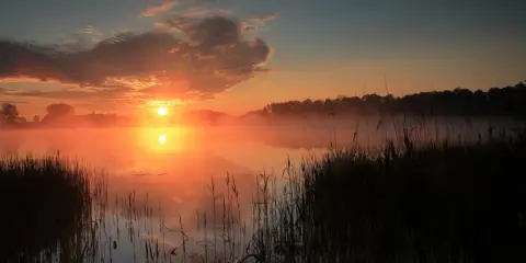 Mglisty poranek na pojezierzu wielkopolskim. Słońce wschodzi nad spokojnymi jeziorami, malując niebo odcieniami pomarańczy i różu.