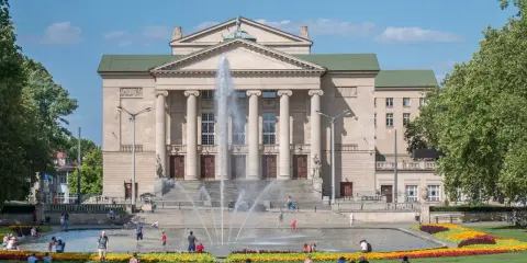 Teatr Wielki w Poznaniu z fontanną i ludźmi odpoczywającymi na trawie to jedne z fajnych miejsc w Poznaniu na spotkanie.