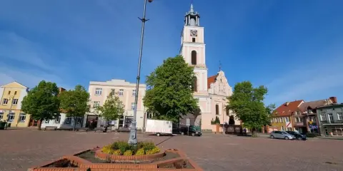 Rynek w Chodzieży Wielkopolskiej z kościołem i kamienicami. Słoneczny dzień, błękitne niebo.