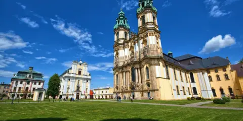 Imponujące, barokowe budowle, w tym jedna z największych bazylik w Polsce, na tle błękitnego nieba z chmurami.