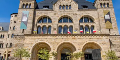 Kamienny pałac cesarski z łukowymi oknami i wieżyczkami. Na fasadzie flagi i banery informujące o Centrum Kultury Zamek i kinie pałacowym.