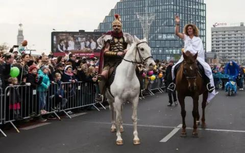 Kiedy jest Marcina, rzymski wojownik na białym koniu i kobieta w bieli na brązowym koniu przejeżdżają przez tłum.