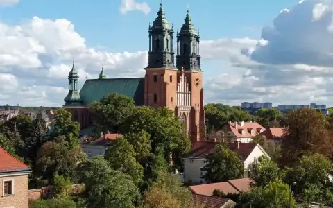 Majestatyczna poznańska katedra z zielonym dachem i dwiema wieżami góruje nad drzewami i budynkami.